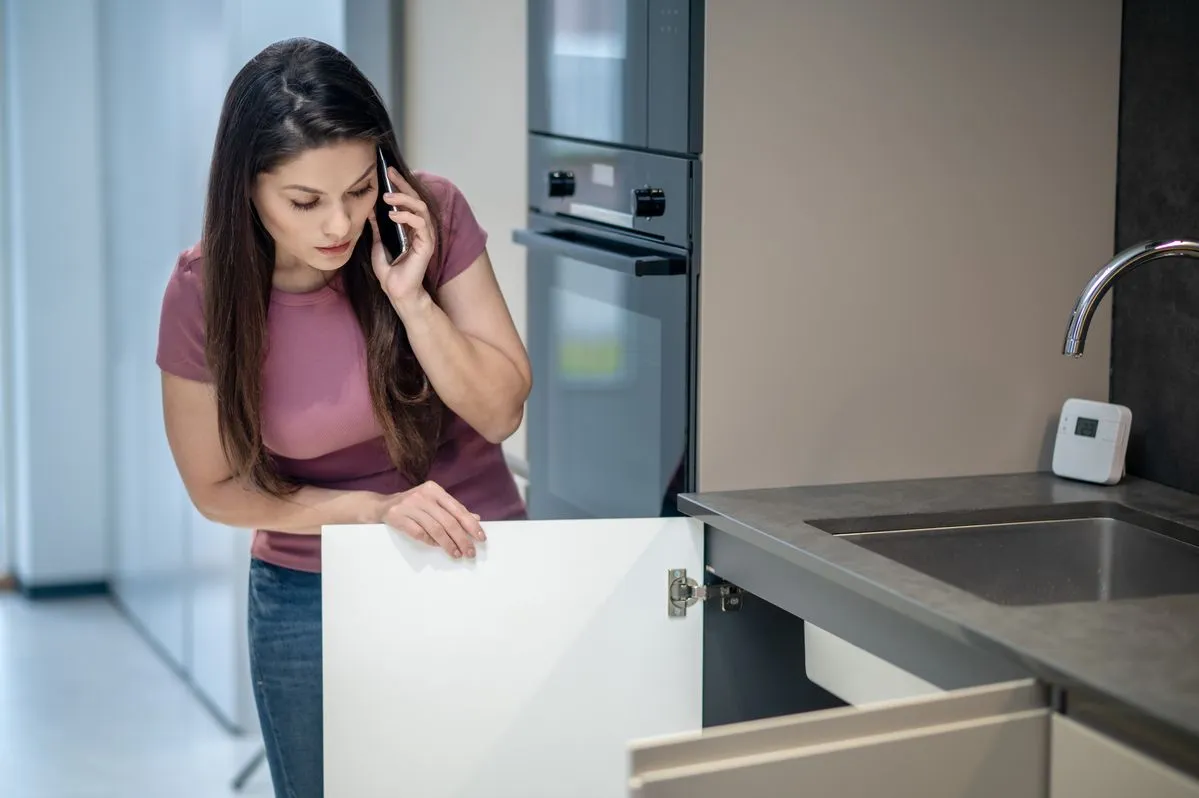 Woman standing in a kitchen, checking the drawer under the sink