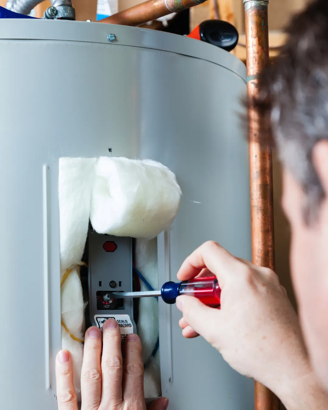 Technician using a screwdriver to service a water heater during routine maintenance